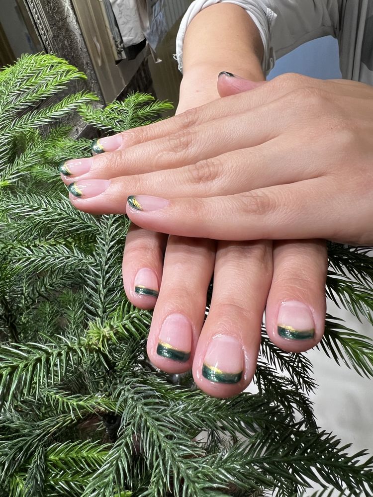 Green and gold French tip nails styled outdoors on pine branches
